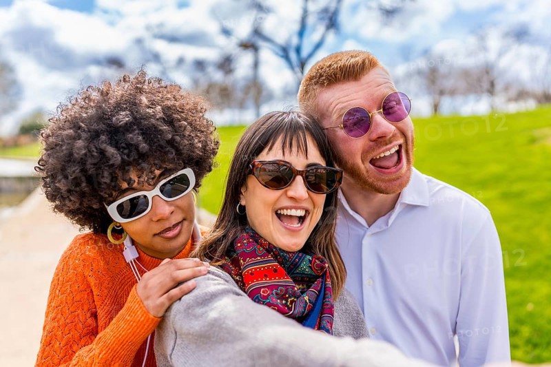 Three cheerful multi ethnic friends are taking a selfie in a park, laughing and enjoying a beautiful sunny day together
