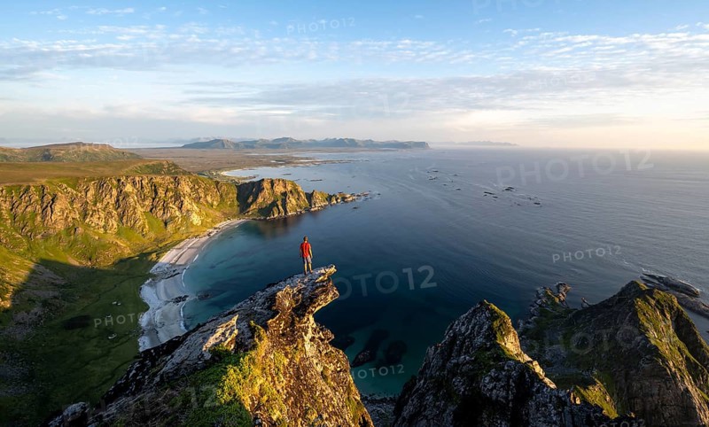Evening mood, mountaineer standing on a rocky outcrop on the summit of Måtind, view of coastal landscape, Høyvika beach and sea, Måtinden, Andøya island, Vesterålen, Nordland Norway