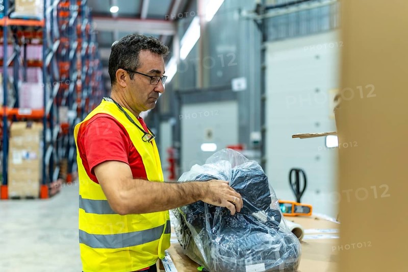 Three quarter length photo of a mature man in waistcoat organizing and taking inventory of objects in a warehouse