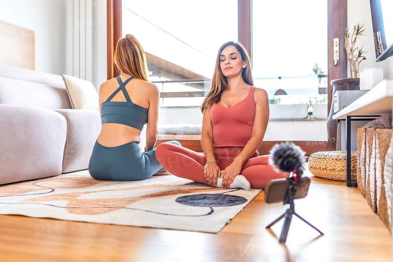 Two women recording an online yoga and meditation class in a cozy living room, embracing wellness and connection through digital content creation