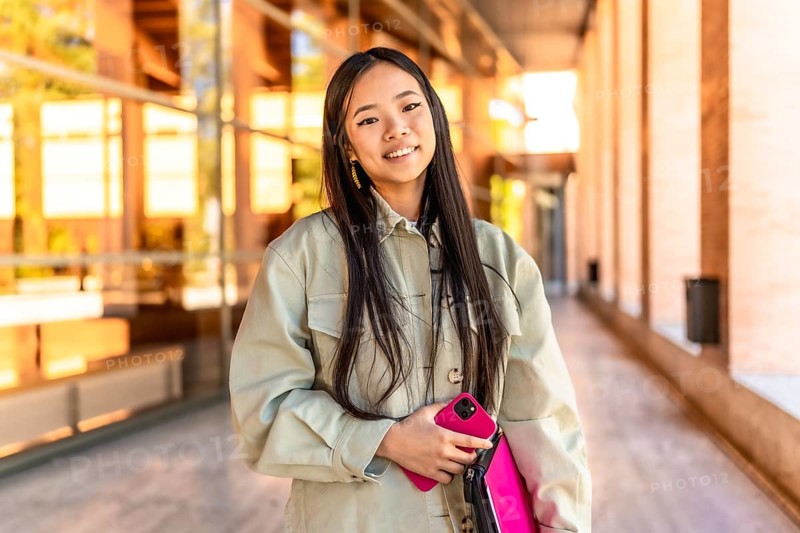 Portrait of a female beauty chinese cute university student standing with mobile phone and laptop