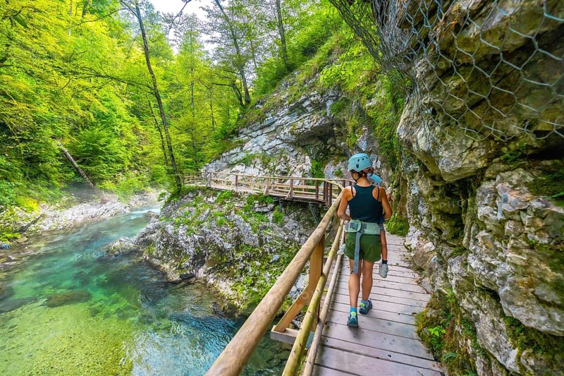 Mother and child enjoying a hike through the scenic vintgar gorge near bled, slovenia, walking along a wooden walkway above a clear, turquoise river