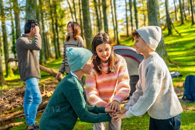 Two caucasian brothers and sister stacking hands playing in the forest enjoying camping with family
