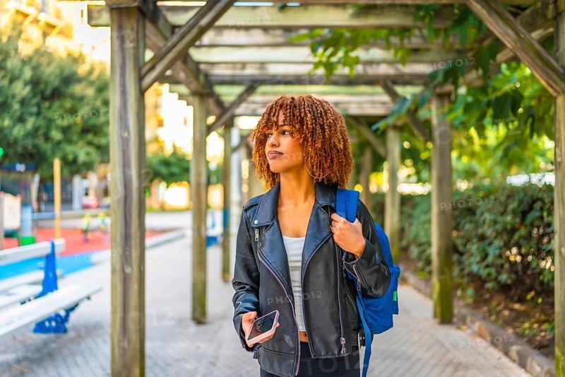 Young latin beauty woman wearing leather jacket walking in the city holding phone