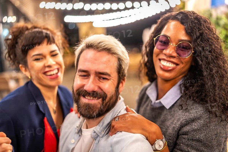 Happy diverse multi-ethnic young friends taking selfie at night party outdoors in a terrace bar
