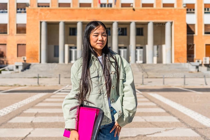 Portrait of a confident chines university student standing in the street at the entrance of the building