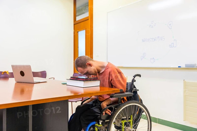 Side view horizontal photo with copy space of a man with cerebral palsy using digital tablet working in coworking