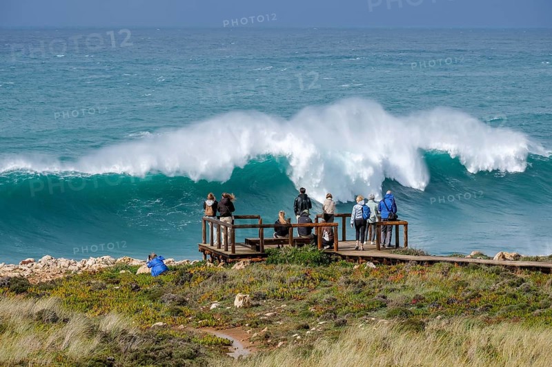Carrapateira, Algarve, Portugal - Tourists on a viewing platform marvel at the roaring surf and spray not far from Praia do Bordeira on a stormy spring day. Carrapateira is a village in the municipality of Bordeira in the south of Portugal. It is located in the Parque Natural do Sudoeste Alentejano e Costa Vicentina, Southwest Alentejo and Costa Vicentina nature park Park