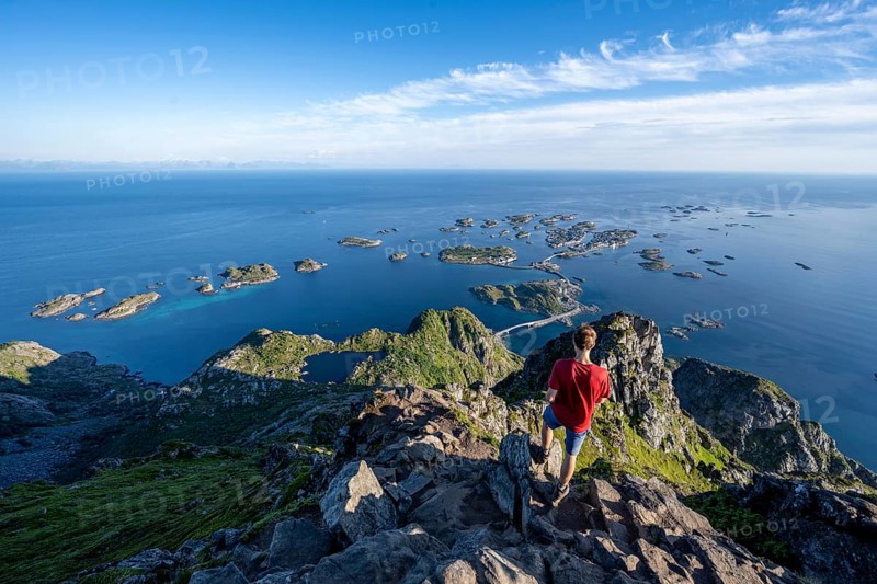 Mountaineer on the summit of Festvagstinden, view of the sea and archipelago islands with the village of Henningsvær, coastal landscape, Lofoten, Nordland, Norway, Europe