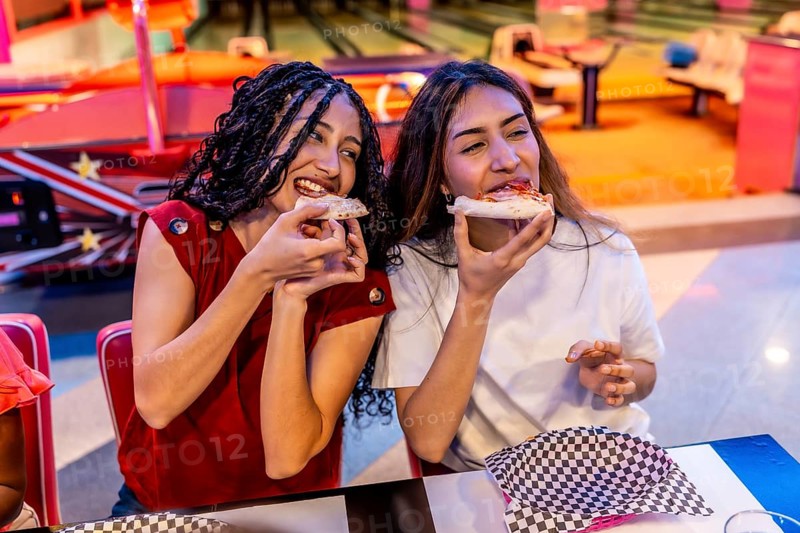 Two joyful young women sharing delicious pizza while enjoying a fun filled day at the bowling alley, creating lasting memories together
