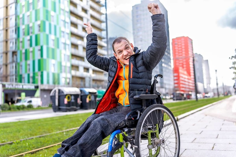 Happy disabled man celebrating in a wheelchair near modern buildings, enjoying his freedom and mobility in the urban environment