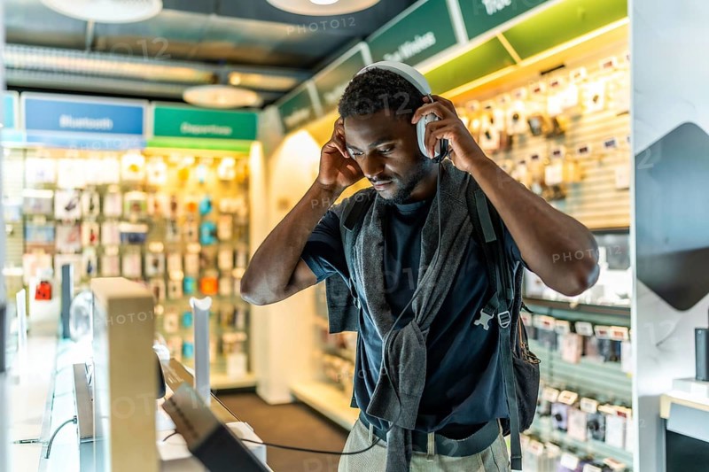 Young african man checking new headphones in electronics store standing alone