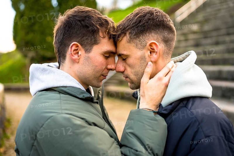 Two men sharing a tender moment, foreheads touching, eyes closed, embracing in a park setting
