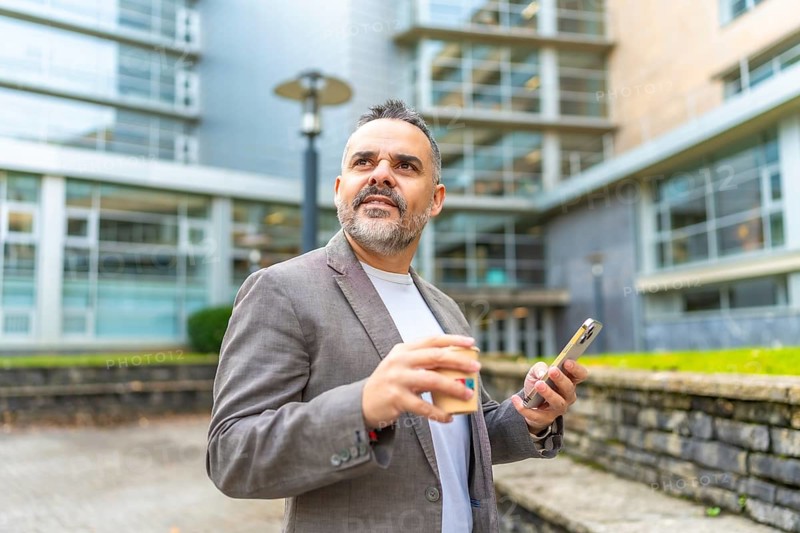Mature caucasian businessman using phone during coffee break outside the office enjoying fresh air