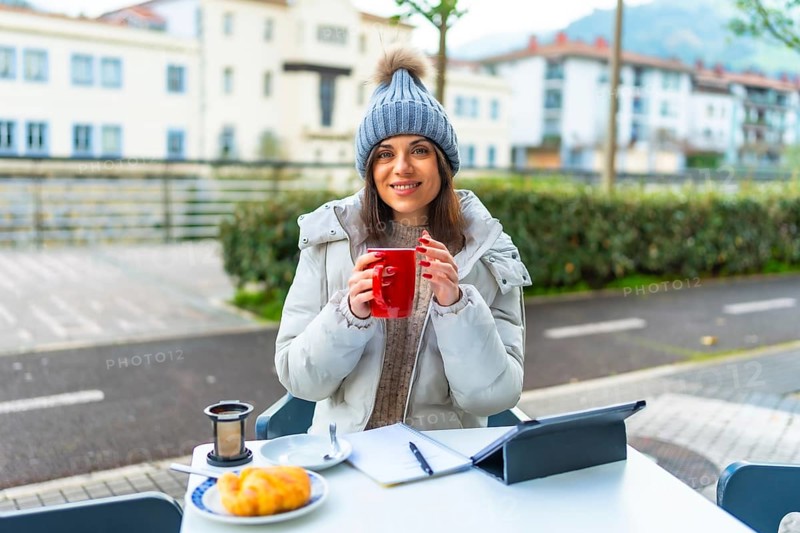 Happy beauty woman enjoying warm tea working with tablet in an outdoor sidewalk cafeteria
