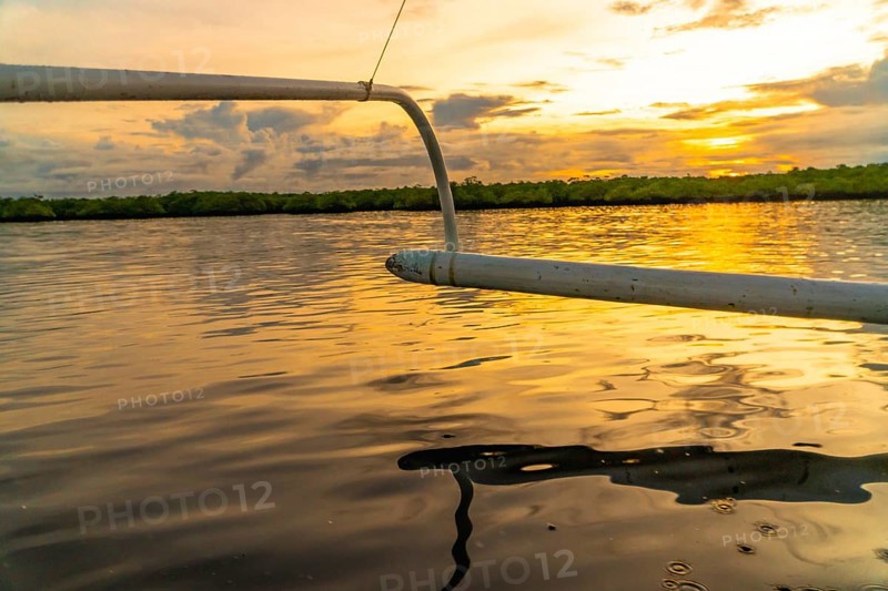 Outrigger of a banca boat sailing on calm water during a golden sunset in siargao island, philippines