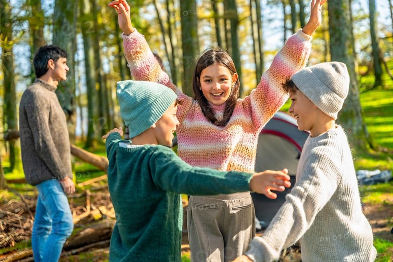 Brothers and sister raising hands after stacking while enjoying a camping day with family in a green alpine forest