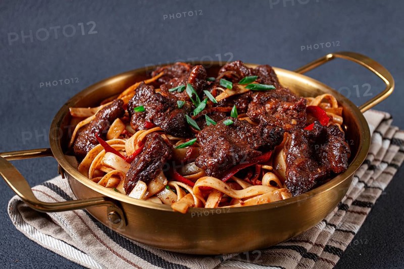 Udon noodles with Mongolian beef, green onions and vegetables, in a brass pan, on a gray background, homemade, no people