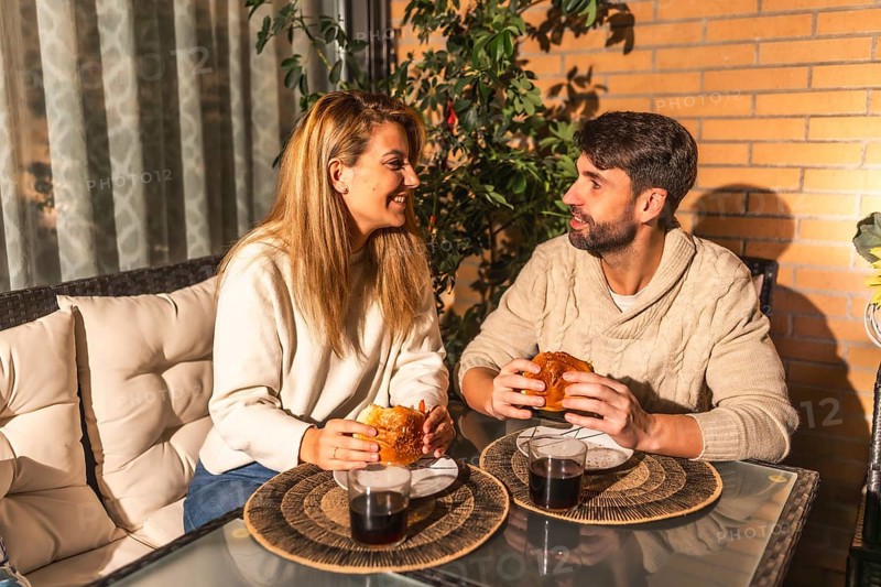 Young couple enjoying a cozy meal and drinks on their balcony, soaking in the warm summer evening and sharing laughter during sunset