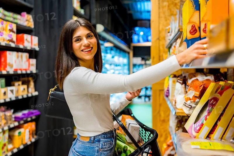 Young woman shopping for groceries, picking a box from the shelf in a supermarket specializing in organic and natural products