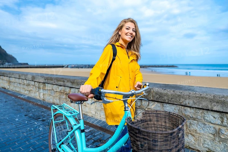 Happy young woman walking with her bicycle on the boardwalk by the beach, enjoying the fresh air and ocean view