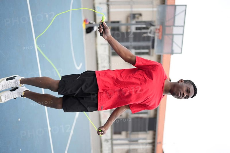 Vertical photo of an energetic african teenager jumping rope in an urban basketball court