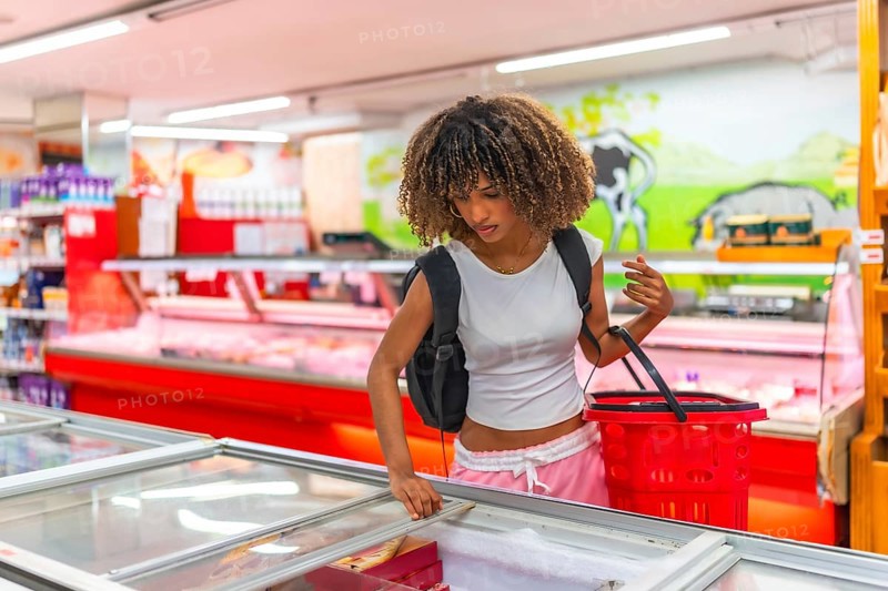 Latin young and beauty woman shopping in the frozen food section of a supermarket holding red basket