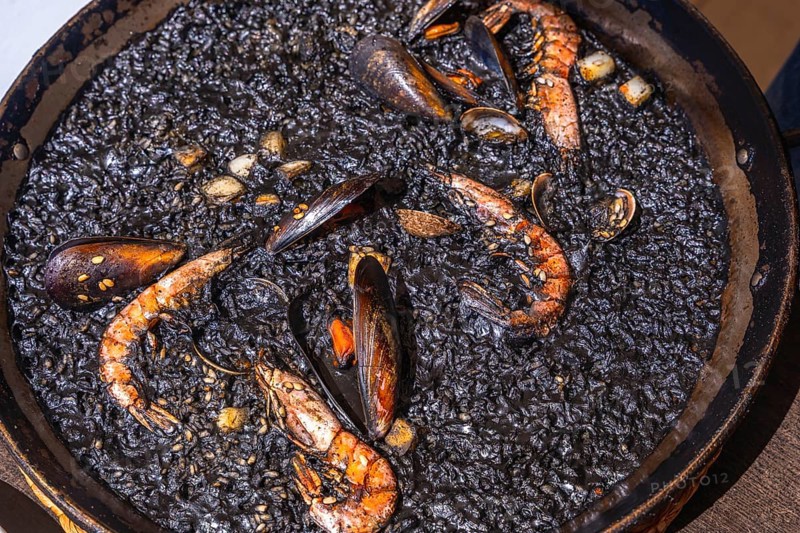 Close up of black paella with shrimps, mussels and other seafood, cooked and ready to be served in a traditional paella pan