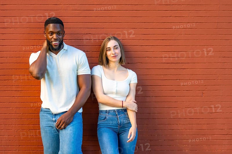 Horizontal photo with copy space of a shy multi-ethnic couple in denim clothes leaning on urban wall together
