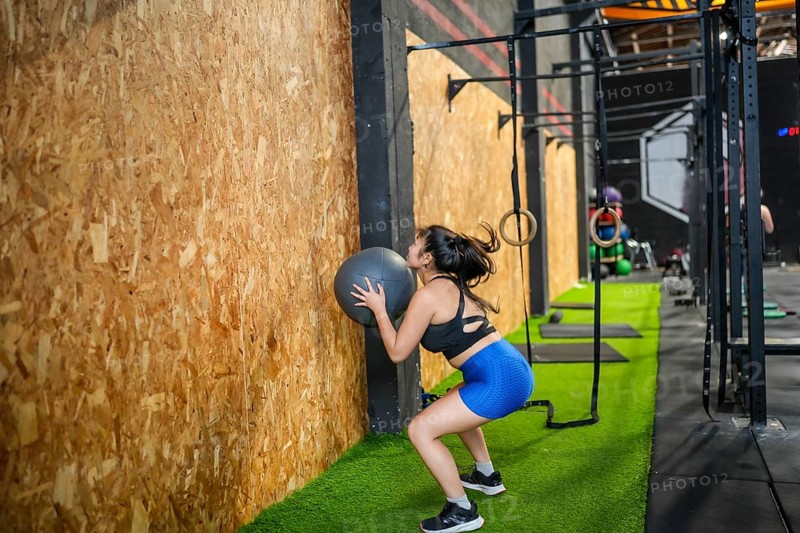 Chinese fit woman training with medicine ball in the gym squatting and throwing up the ball