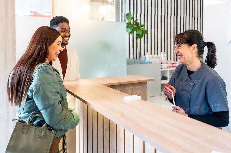 Happy couple engaging with a friendly receptionist in a bright, modern dental clinic, enjoying a positive healthcare experience