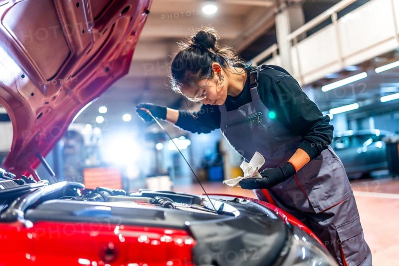 Young female mechanic checking the oil level of a car engine during a maintenance service in a professional workshop