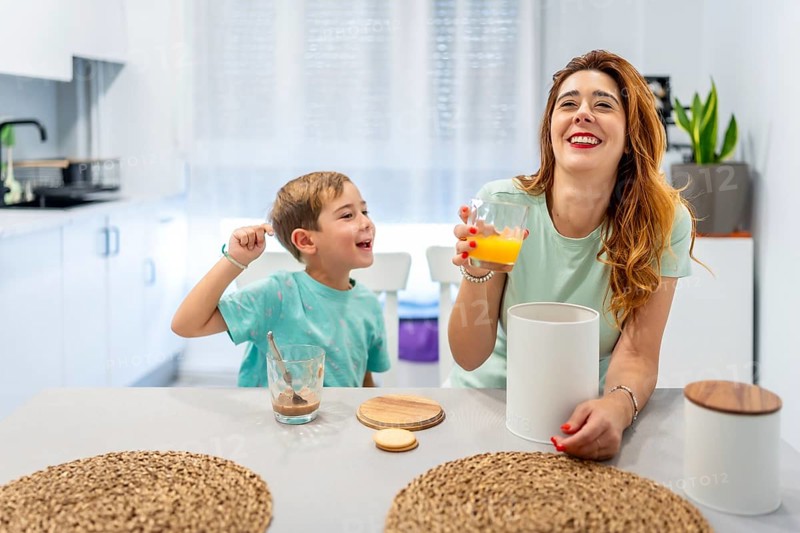 Mother and boy laughing while eating breakfast before going to school at home