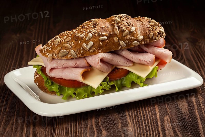 Ham sandwich with lettuce, cheese, tomato on plate on wooden table
