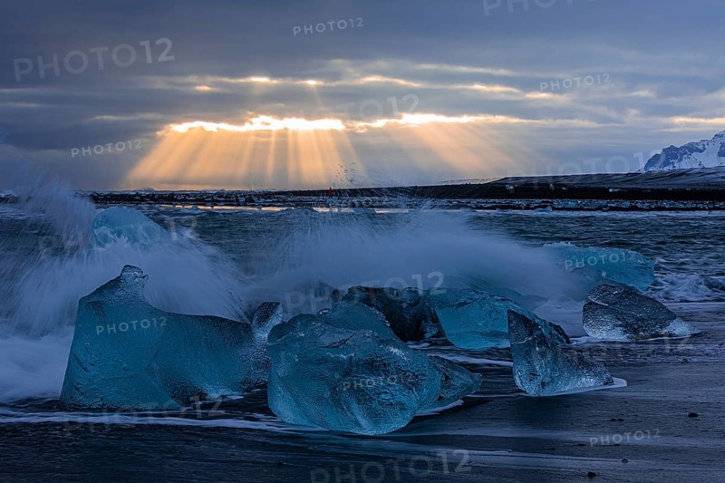 Waves breaking on icebergs on the black beach of Breidamerkursandur, sunset, near Jökullsarlon, Sudurland, Iceland, Europe