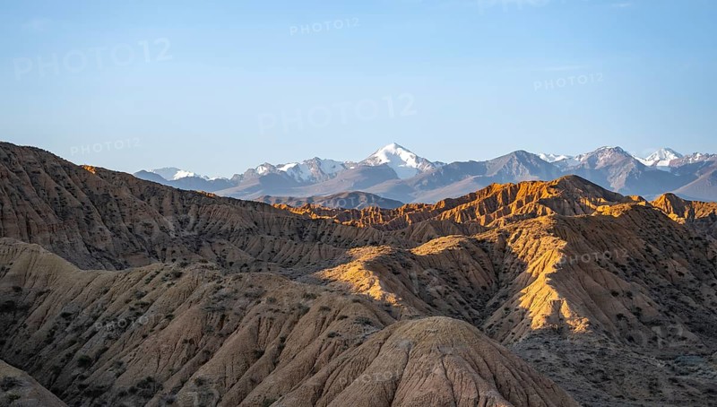 Landscape of eroded hills at sunrise, badlands, white mountain peaks of the Tian Shan Mountains in the background, Canyon of the Forgotten Rivers, Issyk Kul, Kyrgyzstan, Asia
