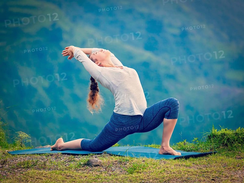 Yoga outdoors, sporty fit woman practices Hatha yoga asana Anjaneyasana, low crescent lunge pose posture outdoors in Himalayas mountains. Vintage retro effect filtered hipster style image
