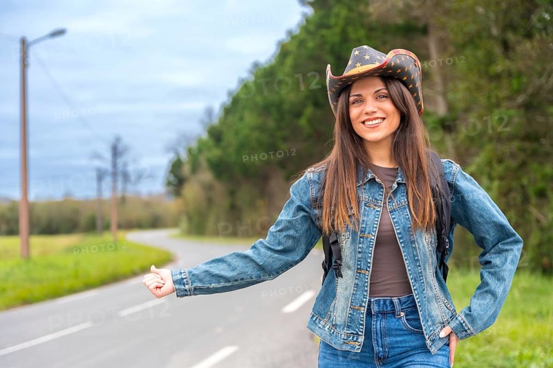 Woman in denim and cowboy hat hitchhiking in a rural road