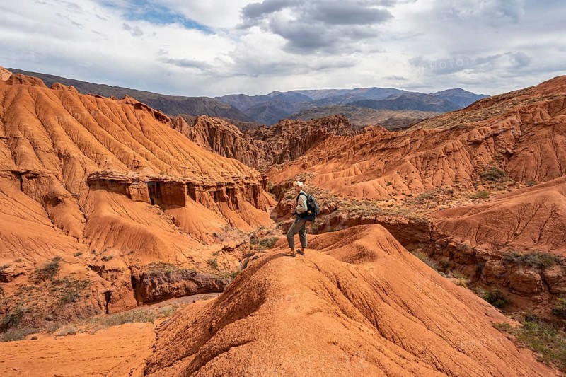 Mountaineer on a mountain ridge, view of eroded mountain landscape with sandstone cliffs, canyon with red and orange rock formations, Konorchek Canyon, Chuy, Kyrgyzstan, Asia