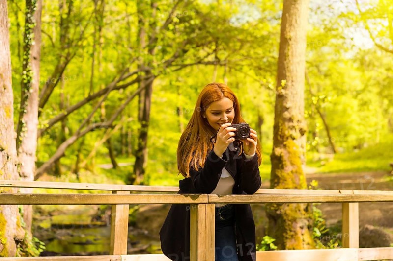 Woman photographer with a black jacket enjoying in an autumn park, taking pictures on a wooden bridge