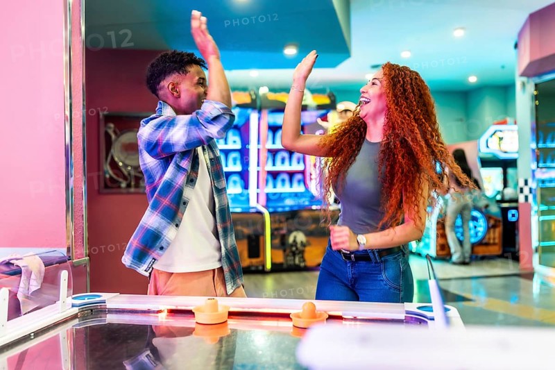 Two friends giving high five while enjoying a game of air hockey in a vibrant entertainment center, celebrating a point or victory
