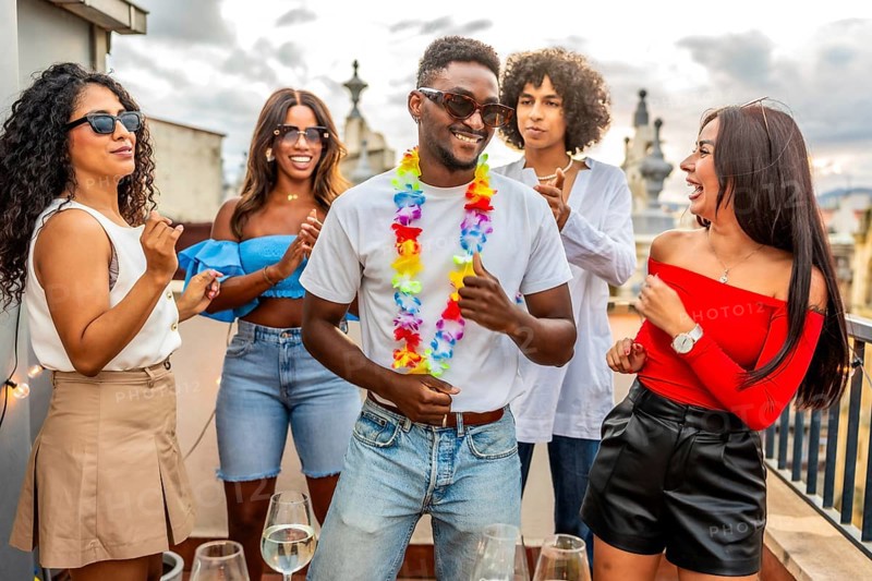 Happy latin man with Hawaiian necklace dancing with friends in outdoor rooftop party