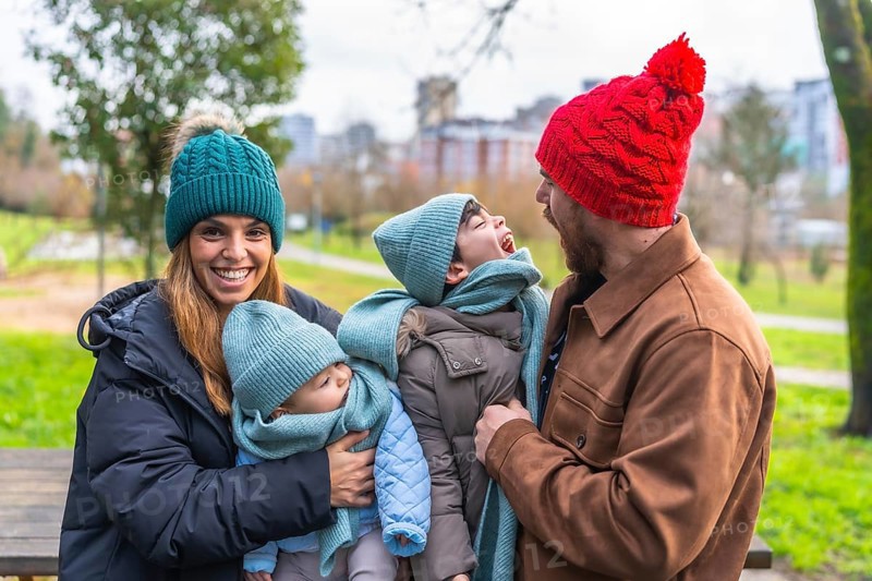 Happy family enjoying a winter day together in a park, wearing warm clothes and woolen hats