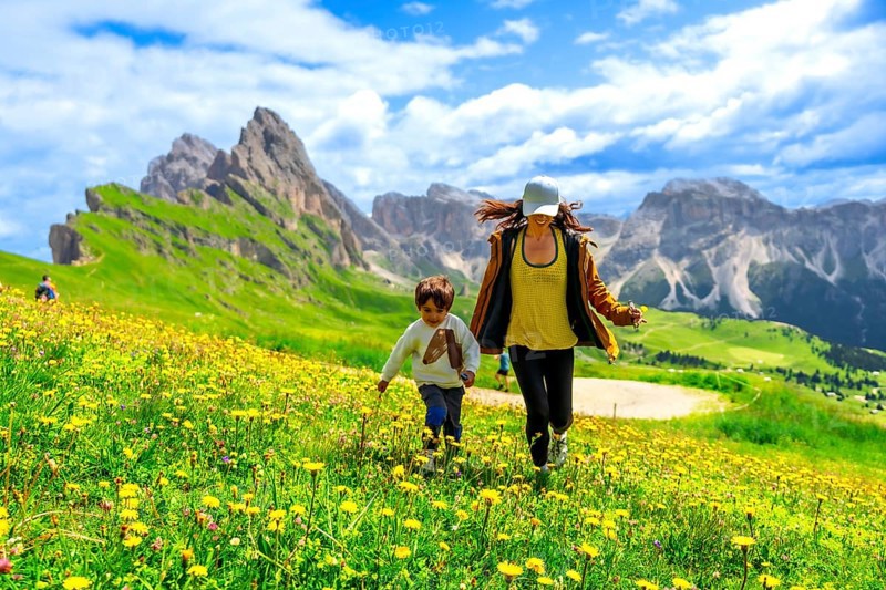 Mother and son running through a field of wildflowers in the italian dolomites mountains, enjoying summer vacation in the seceda region