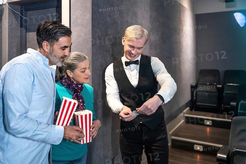 Couple entering a movie theater, holding popcorn buckets while the usher checks their tickets, enjoying a casual and happy evening together