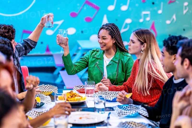 Multiethnic friends enjoying a meal and drinks at a bowling alley restaurant, celebrating their weekend together