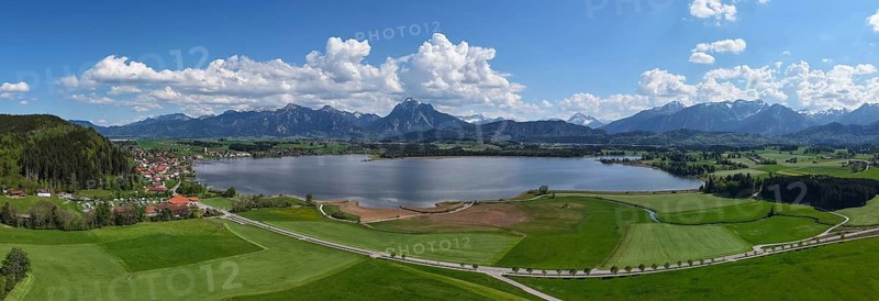 Expansive landscape with a view of Lake Hopfensee and mountains, surrounded by green meadows and a blue sky with clouds, Alps, Hopfen am See near Füssen, Ostallgäu, Allgäu, Bavaria, Germany, Europe