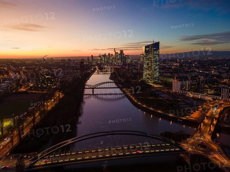 The lights in the offices of the European Central Bank (ECB) and in the skyscrapers of Frankfurt's banking skyline glow in the evening shortly after sunset. (Aerial view with a drone), Frankfurt am Main, Osthafen, Hesse, Germany, Europe
