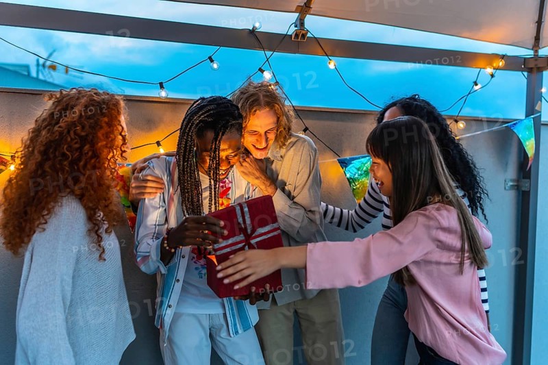 Happy millennial multi-ethnic friends celebrating birthday party in an urban rooftop at dusk