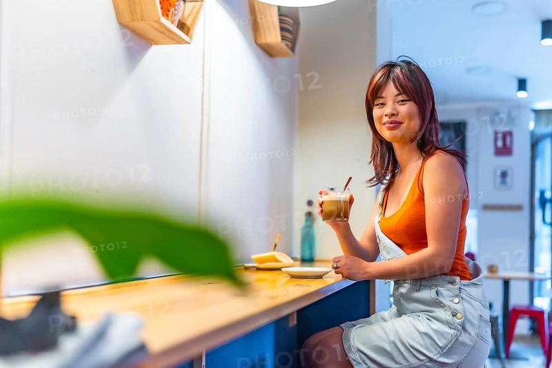 Portrait with copy space of a smiling asian youthful woman drinking coffee in a cafeteria